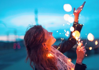 Happy woman playing with fairy light garland at evening